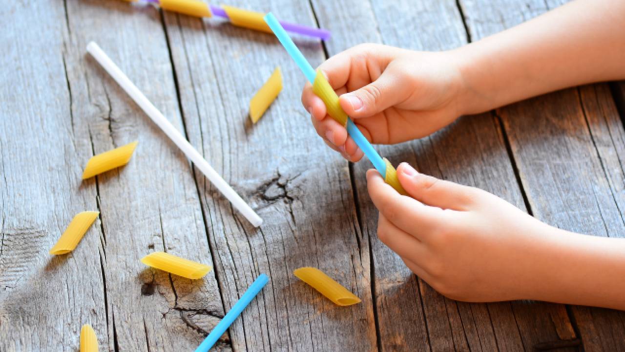 child threading maccaroni onto a straw