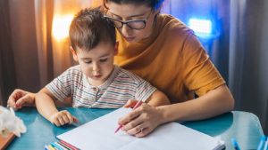 Preschooler being helped to write by their parent