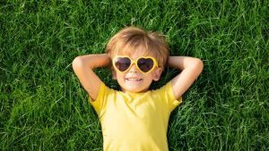 A preschooler laying on the grass with a yellow shirt and yellow sunglasses on
