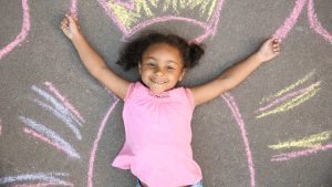 A girl in a pink dress laying on the ground with chalk lines imitating wings