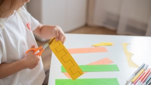 Child engaging in a cutting activity using scissors to cut along the lines on a piece of paper